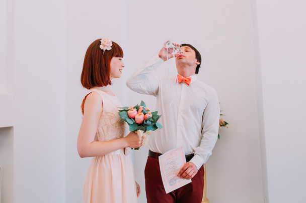 Gelukkig jonggehuwden op hun ceremonie van het huwelijk in registratiekantoor drinken van wijn en vieren - Foto, afbeelding
