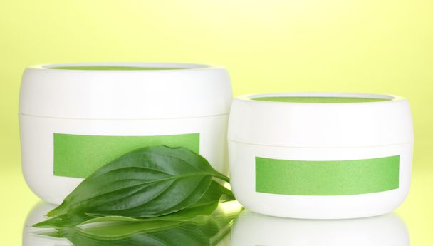 Jars of cream with green leaves on green background - Photo, image