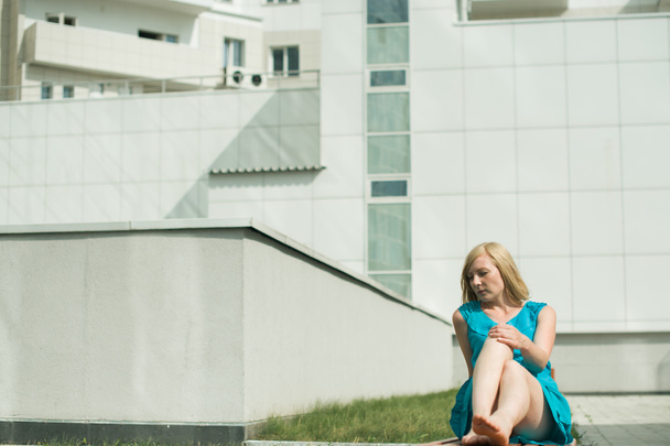 young blond woman sitting on a bench in the courtyard stretching her legs - Photo, Image