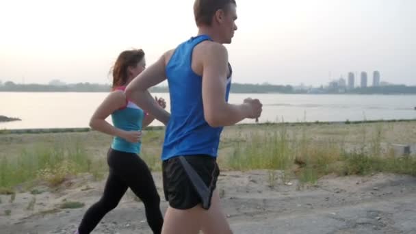 Paar junger erwachsener Sportler: Frau und Mann, die entlang der Uferpromenade des Flusses laufen. gesundes Lebensstilkonzept, Zeitlupe, Rückansicht - Filmmaterial, Video
