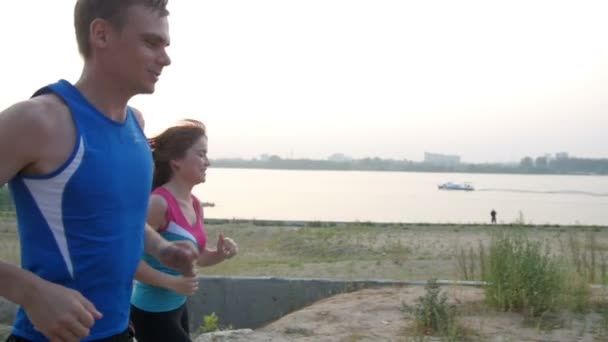 Paar junger erwachsener Sportler: Frau und Mann, die entlang der Uferpromenade des Flusses laufen. gesunder Lebensstil, Zeitlupe - Filmmaterial, Video