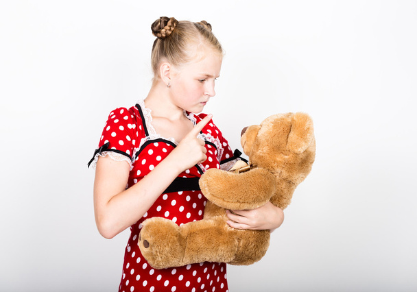 beautiful young girl dressed in a red dress with white polka dots holding a teddy bear - Fotó, kép