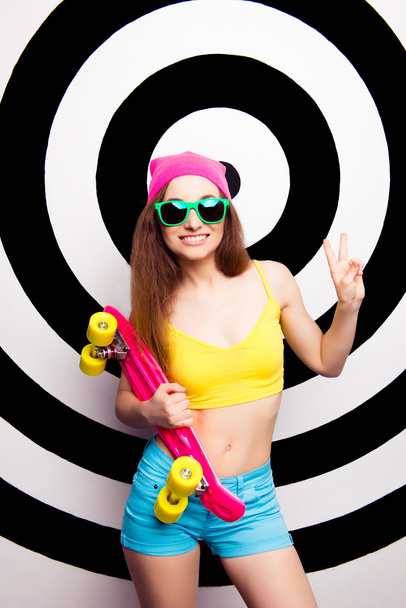 Hipster cute cool girl in glasses holding skate and smiling - 写真・画像