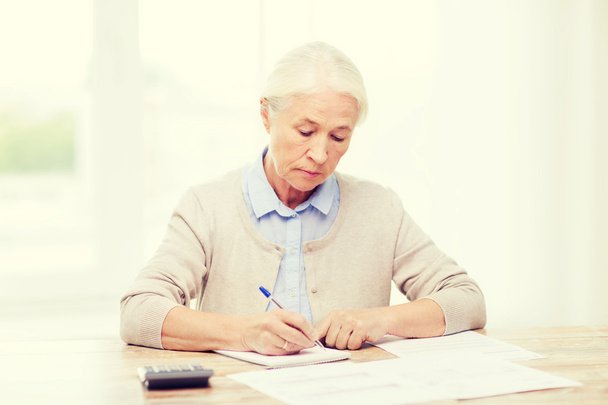 senior woman with papers and calculator at home - Foto, Bild