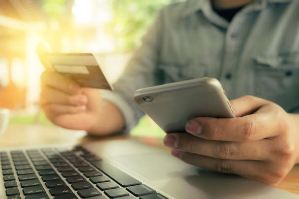 Online fizetés, az ember keze kezében egy hitelkártya és használ okos telefon az online vásárlás a reggeli fényben. Vintage szűrőhatás. - Fotó, kép