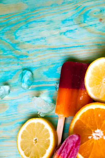 Colorful ice lolly and friuts on blue wooden background - Foto, afbeelding