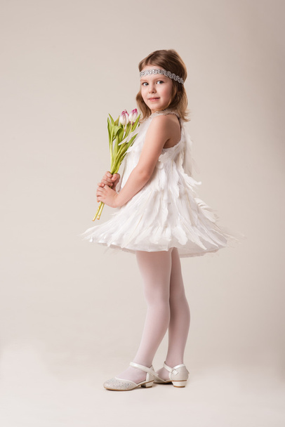 Porträt eines schönen, fröhlichen Mädchens in einem Kleid aus weißen Federn, mit Blumen in den Händen - Foto, Bild