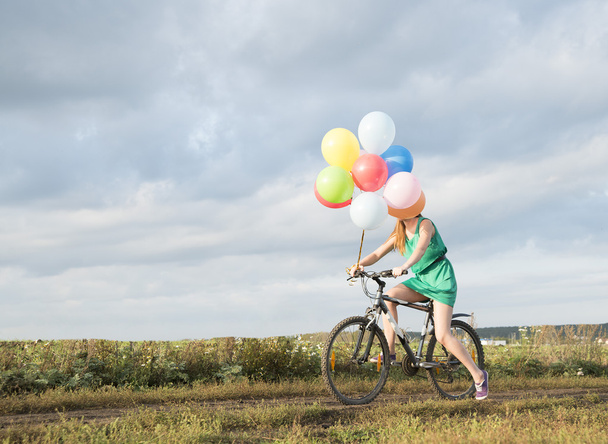 woman riding bicycle and holding balloons - Photo, Image