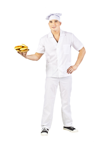 Attractive man in white uniform  carrying a bowl of freshly baked cookies isolated on white - Foto, afbeelding