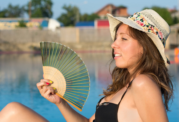Девушка в бикини держит веер у бассейна
 - Фото, изображение