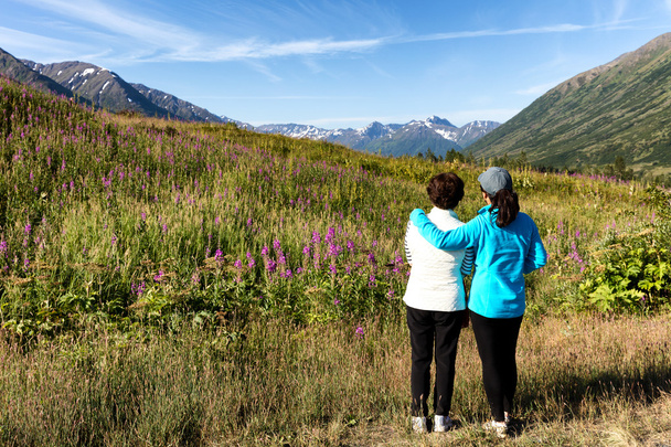 Μητέρα και κόρη να βλέπουν άγρια λουλούδια με βουνά και στ - Φωτογραφία, εικόνα
