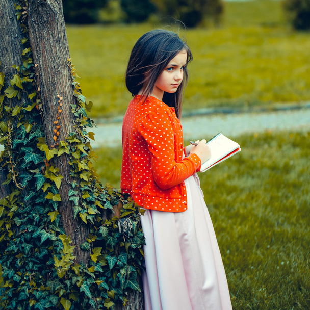 Κορίτσι στο φόρεμα με σημειωματάριο και στυλό κοντά στο δέντρο - Φωτογραφία, εικόνα