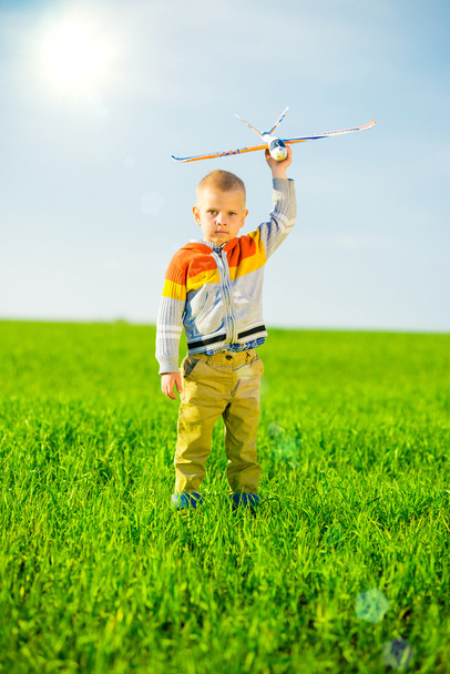 Happy boy playing with toy airplane against blue summer sky and green field background. - Foto, immagini