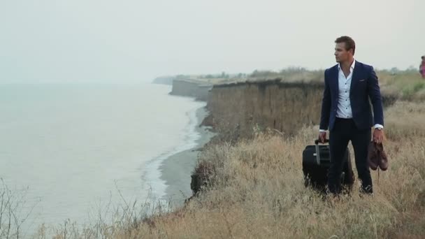 Homme d'affaires avec un sac de voyage près d'une falaise au bord de la mer
. - Séquence, vidéo