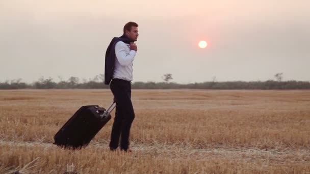 A man in a business suit comes with a travel bag on a field of harvested wheat. - Footage, Video