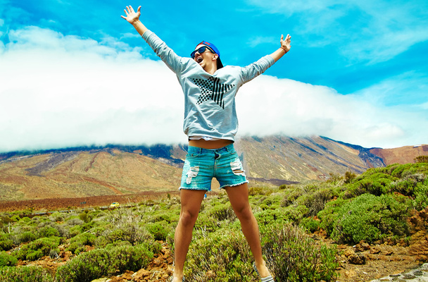 Happy stylish man in casual hipster clothes jumping in front of mountain with raised hands to the sun and celebrating success - Фото, зображення
