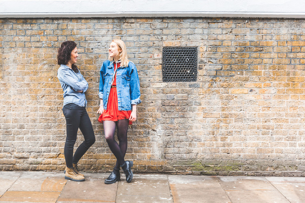 Two women leaning on a wall and talking in London - Foto, imagen