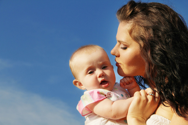 Happy mother kissing baby over blue sky - Photo, image