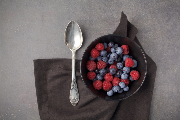Blueberries and raspberries in a bowl on rusty grey background. Top view - 写真・画像