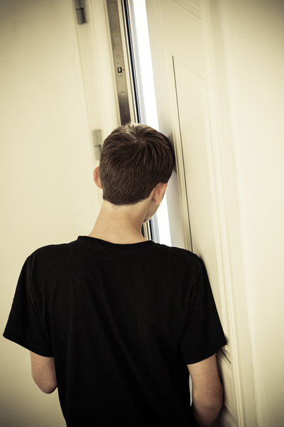 Achteraanzicht van tiener scheve hoofd tegen muur - Foto, afbeelding