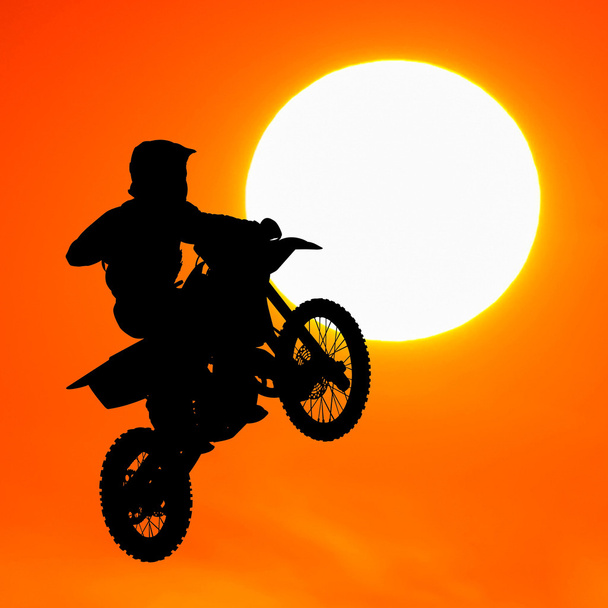 Silhouette des Motocross-Fahrers springt bei Sonnenuntergang in den Himmel - Foto, Bild