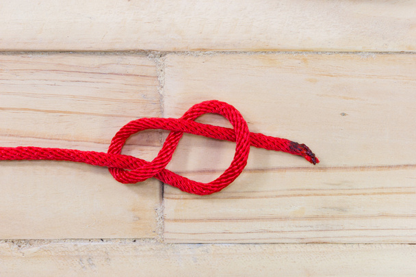 Figure-eight knot made with red rope on wooden background - Foto, imagen