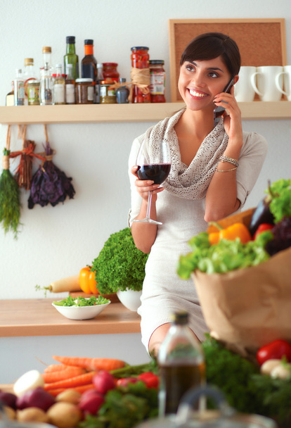 Young woman cutting vegetables in kitchen, holding a glass of wine - Photo, image