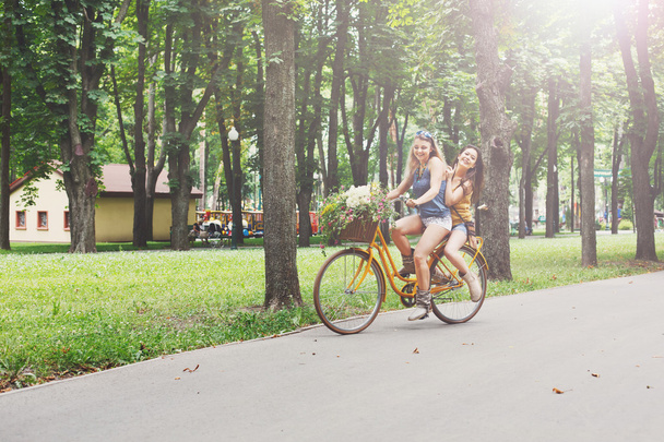 glücklich Boho Chic Mädchen fahren zusammen auf Fahrrädern im Park - Foto, Bild
