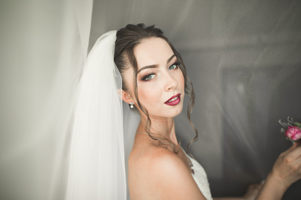 Beautiful young bride with makeup and hairstyle in bedroom, newlywed woman final preparation for wedding. Happy girl waiting groom. Portrait soft focus - Фото, изображение