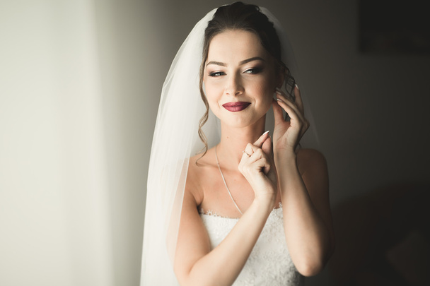 Beautiful young bride with makeup and hairstyle in bedroom, newlywed woman final preparation for wedding. Happy girl waiting groom. Portrait soft focus - 写真・画像