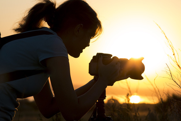 silhouette portrait of a young woman photographing a beautiful nature at sunset on photo equipment - Φωτογραφία, εικόνα