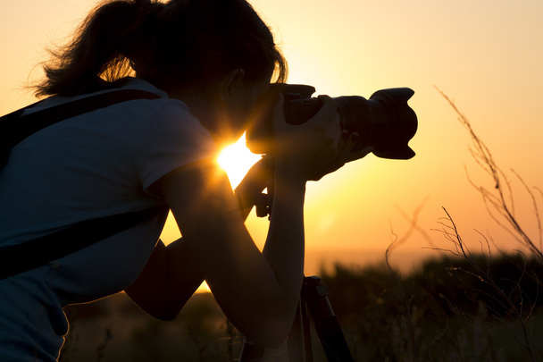 silhouette portrait of a young woman photographing a beautiful nature at sunset on photo equipment - Foto, Imagem