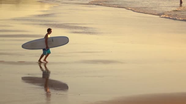 Lassú mozgás: Mosolygó fiatal szörfös óceánba szörfdeszka kezében fut - Felvétel, videó