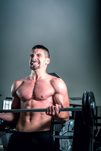 Young man doing barbell exercise in gym - Photo, image