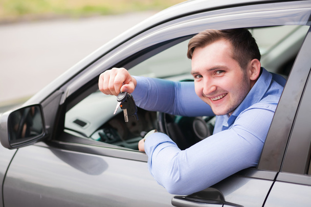 młody człowiek siedzący w samochodzie gospodarstwa kluczyki do samochodu - Zdjęcie, obraz