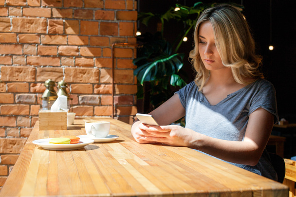 Jong meisje lezen iets op slimme telefoon in de coffeeshop - Foto, afbeelding