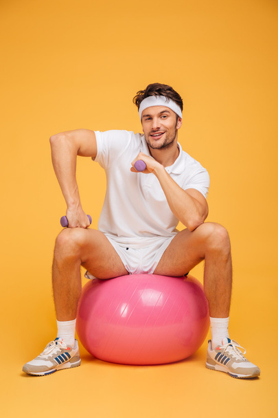 ダンベルを持つフィットネスボールに座って笑顔のスポーツマン - 写真・画像