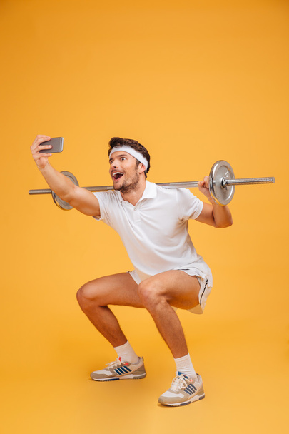 Happy man athlete working out with barbell and making selfie - Фото, изображение
