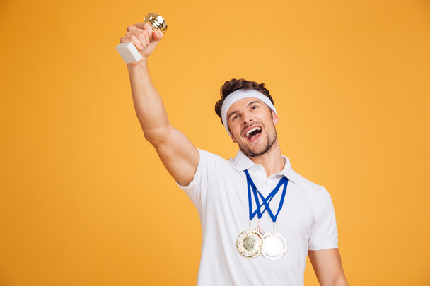 Happy man athlete with medals and trophy cup celebrating victory - Foto, imagen