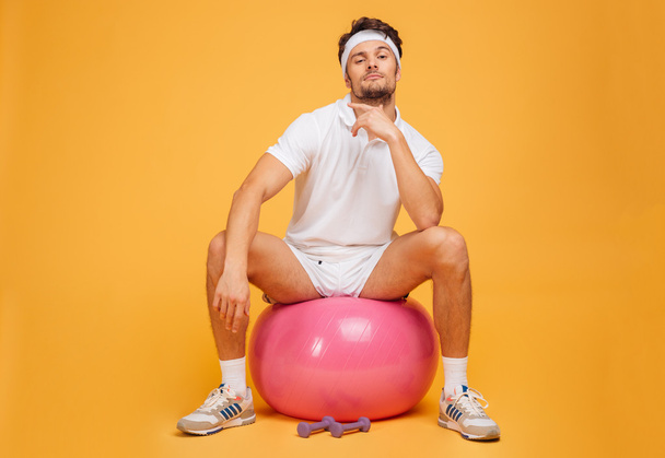 Handsome young sportsman sitting on the fitness ball - Фото, зображення
