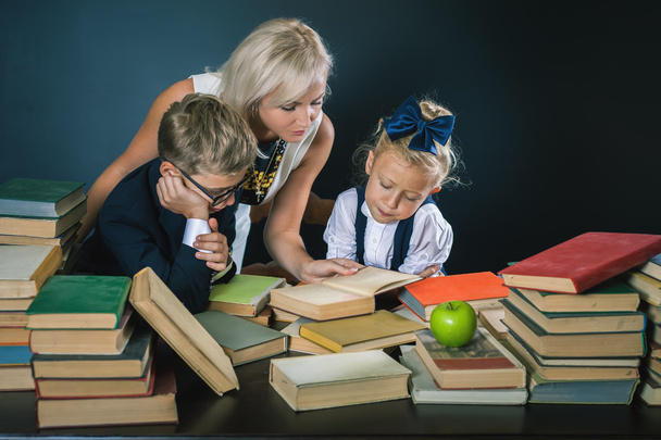 Madre o maestra ayudando a los niños de la escuela a hacer los deberes, leyendo
 - Foto, Imagen