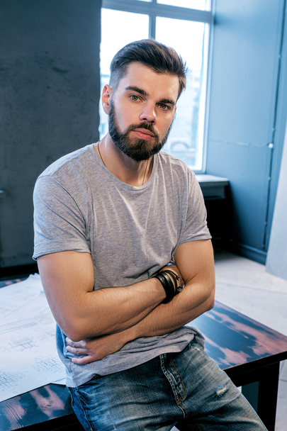 Portrait of young good-looking man with arms crossed leaning on desk in office - Photo, Image