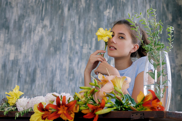 Portrait of young brunette girl holding yellow flower at face.Textured wall on background - Photo, Image