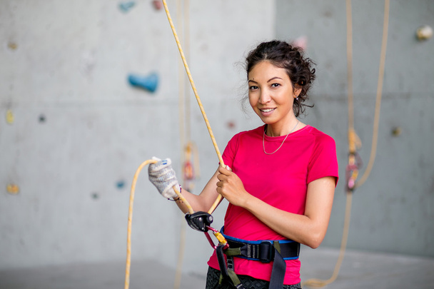 Retrato de la hermosa mujer escaladora de roca que cruza a otro escalador con cuerda. Pared y equipo de escalada artificial interior
. - Foto, Imagen