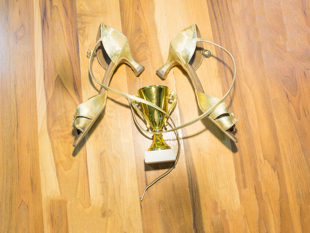 Staré latinské taneční boty na dřevěné podlaze pozadí a zlatý pohár vítěze - Fotografie, Obrázek