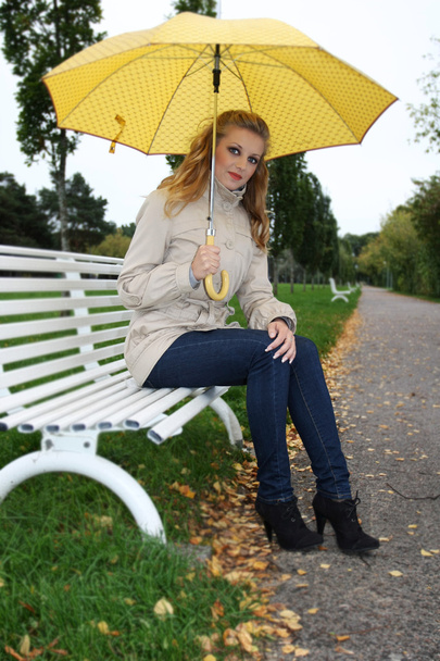 γυναίκα με κίτρινο ομπρέλα που κάθεται σε παγκάκι - Φωτογραφία, εικόνα