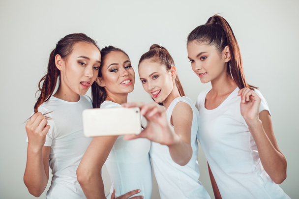 Amigos positivos retrato de cuatro chicas felices haciendo selfie, caras divertidas seguro, muecas, alegría, emociones, estilo casual, colores pastel, pared blanca. Una mujer loca y divertida. Fondo blanco
. - Foto, Imagen