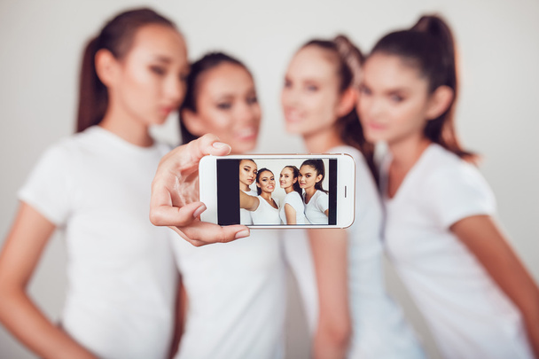 Amigos positivos retrato de cuatro chicas felices haciendo selfie, caras divertidas seguro, muecas, alegría, emociones, estilo casual, colores pastel, pared blanca. Una mujer loca y divertida. Fondo blanco
. - Foto, Imagen