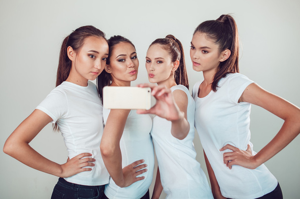 Positive friends portrait of four happy girls making selfie, sure funny faces, grimaces, joy, emotions, casual style, pastel colors, white wall. crazy funny woman. White background. - Photo, image