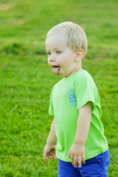舌を示す小さな金髪の少年の肖像画夏屋外 - 写真・画像